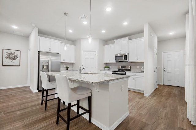 kitchen featuring appliances with stainless steel finishes, a kitchen breakfast bar, wood finished floors, white cabinets, and a sink