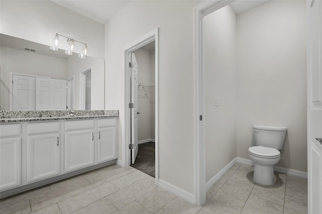 bathroom with vanity, baseboards, visible vents, a walk in closet, and toilet