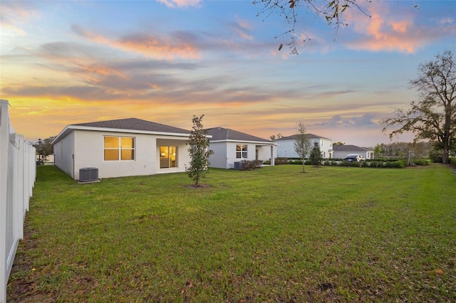 rear view of property featuring a yard, stucco siding, central AC, and fence