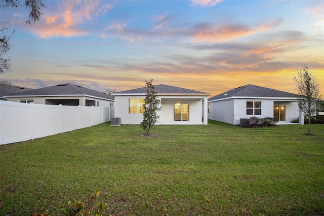 back of property with stucco siding, central AC unit, a yard, and fence