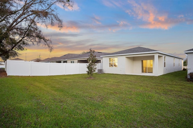 back of house with central AC unit, stucco siding, a lawn, and fence