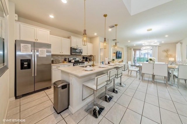 kitchen with sink, white cabinetry, hanging light fixtures, stainless steel appliances, and a kitchen island with sink