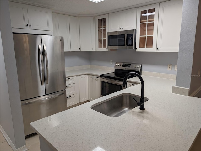 kitchen with stainless steel appliances, white cabinetry, light stone countertops, and sink