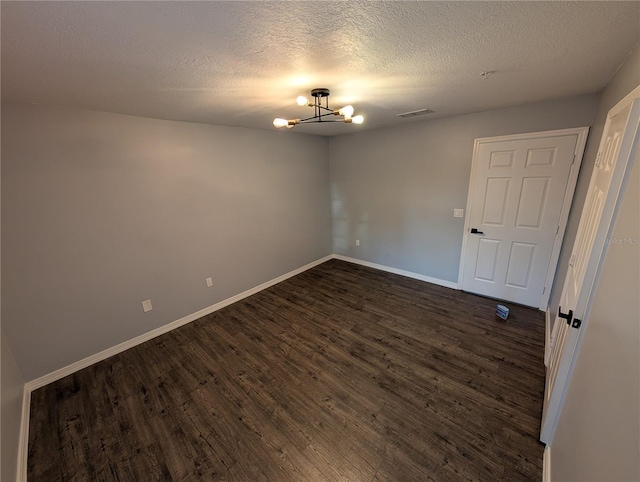 empty room featuring an inviting chandelier, dark hardwood / wood-style flooring, and a textured ceiling