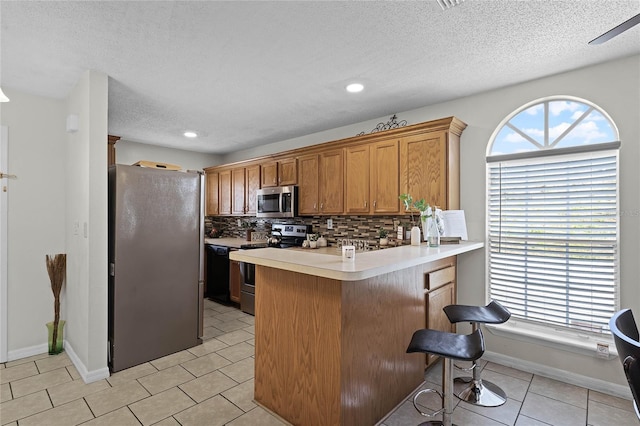 kitchen with appliances with stainless steel finishes, tasteful backsplash, a kitchen bar, light tile patterned flooring, and kitchen peninsula