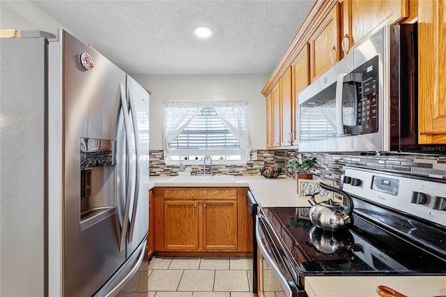 kitchen with sink, light tile patterned floors, stainless steel appliances, tasteful backsplash, and a textured ceiling