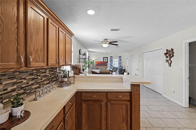 kitchen featuring light tile patterned floors, ceiling fan, a textured ceiling, decorative backsplash, and kitchen peninsula