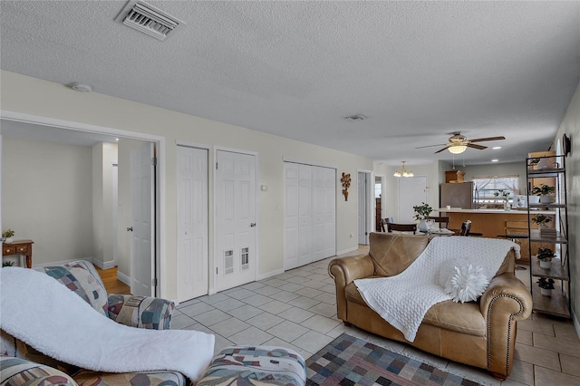 tiled living room with ceiling fan with notable chandelier and a textured ceiling