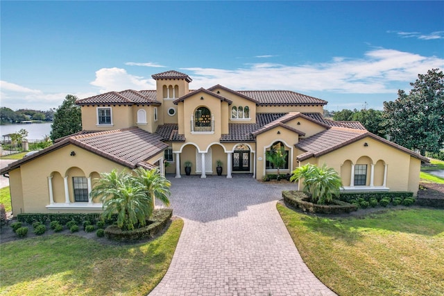 mediterranean / spanish house with decorative driveway, stucco siding, a front lawn, and a tile roof