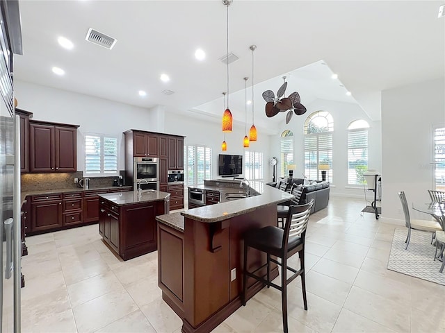 kitchen with sink, hanging light fixtures, an island with sink, vaulted ceiling, and dark stone counters