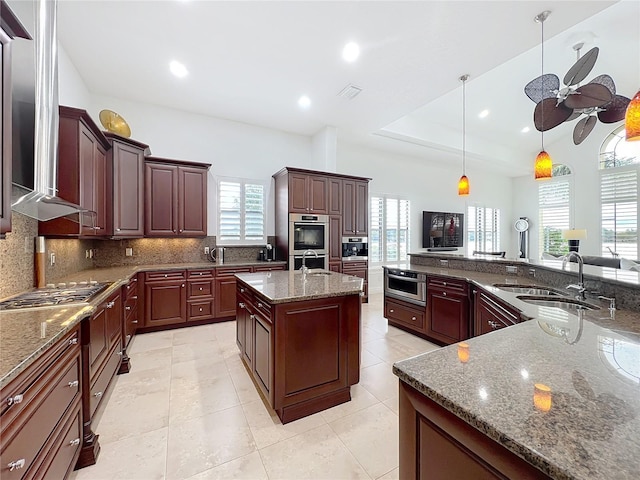 kitchen with sink, tasteful backsplash, hanging light fixtures, a kitchen island, and stone counters