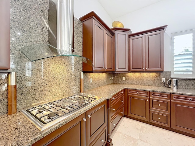 kitchen featuring tasteful backsplash, light stone countertops, wall chimney range hood, and stainless steel gas stovetop