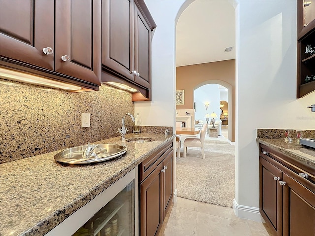 kitchen featuring dark brown cabinetry, sink, light stone counters, light colored carpet, and backsplash