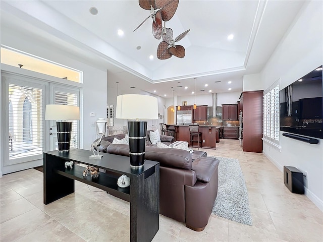 living room with a raised ceiling, vaulted ceiling, and ceiling fan