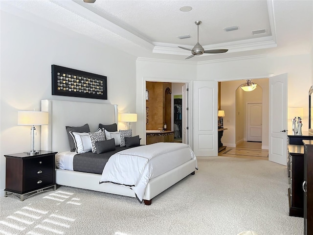 bedroom featuring a raised ceiling, light colored carpet, ceiling fan, and ensuite bath