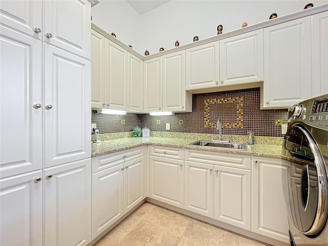 kitchen with sink, backsplash, light stone countertops, white cabinets, and washer / clothes dryer