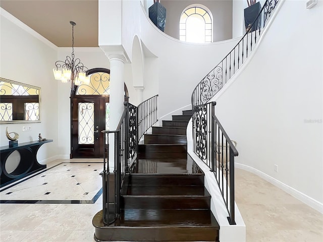 foyer featuring ornate columns, crown molding, a towering ceiling, and a chandelier