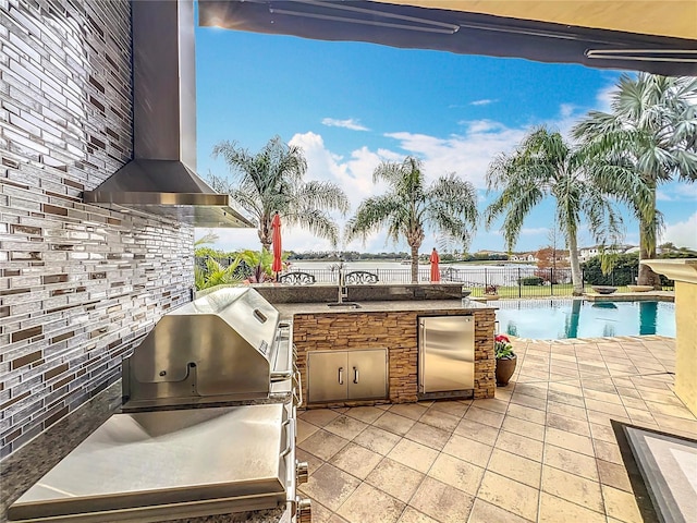 view of patio / terrace featuring exterior kitchen, a grill, a water view, and sink