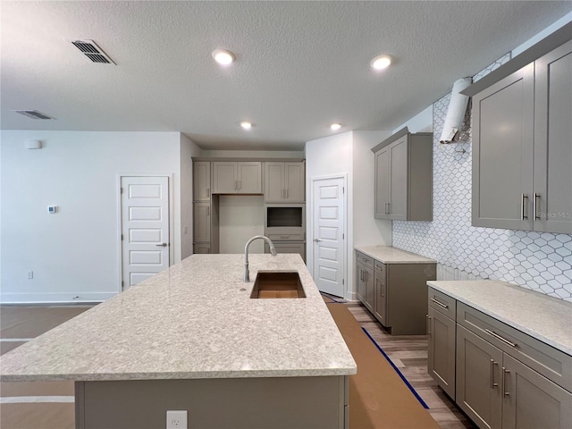 kitchen with visible vents, decorative backsplash, gray cabinets, wood finished floors, and a sink