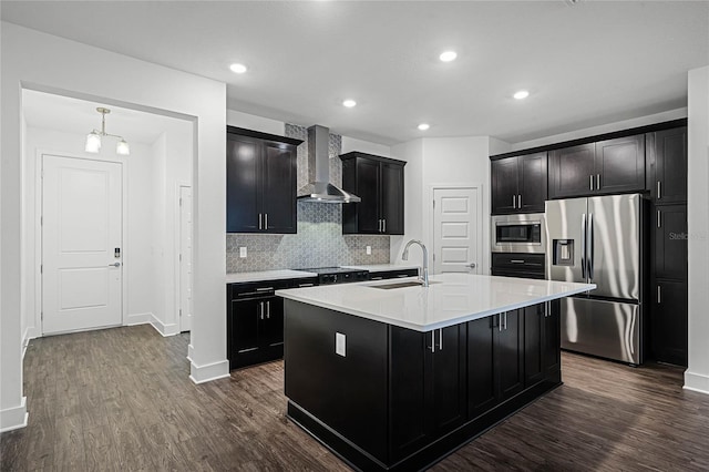 kitchen featuring dark cabinetry, dark wood-style flooring, a sink, appliances with stainless steel finishes, and wall chimney range hood