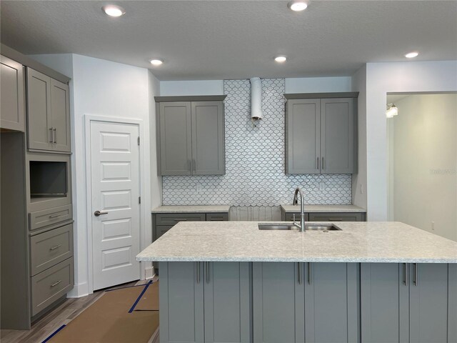 kitchen featuring a kitchen island with sink, gray cabinets, backsplash, and a sink