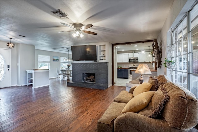 living room with a fireplace, a textured ceiling, dark wood-type flooring, and ceiling fan