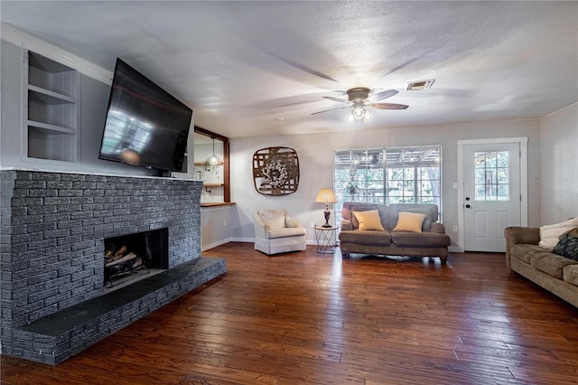 living room featuring a brick fireplace, dark wood-type flooring, a textured ceiling, and ceiling fan