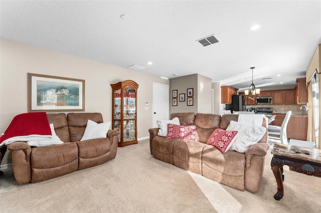 living room featuring an inviting chandelier, light colored carpet, sink, and a textured ceiling