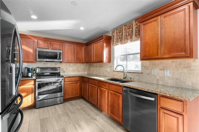 kitchen featuring sink, light hardwood / wood-style flooring, backsplash, stainless steel appliances, and light stone counters