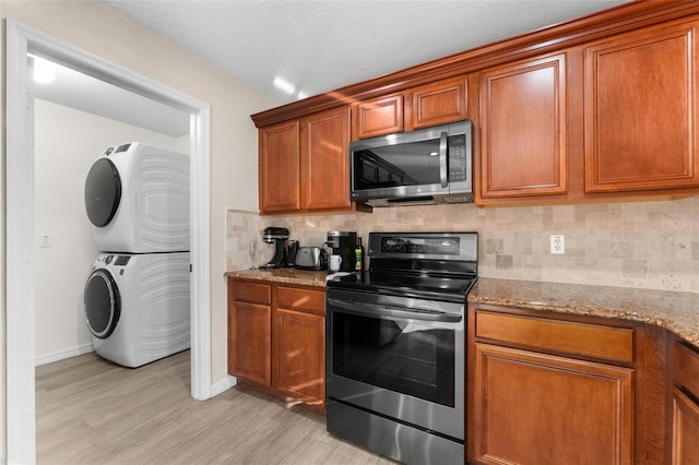 kitchen with light stone counters, stacked washer / dryer, light wood-type flooring, stainless steel appliances, and backsplash