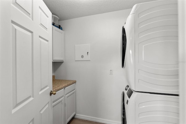 laundry room featuring cabinets, stacked washer / drying machine, and a textured ceiling