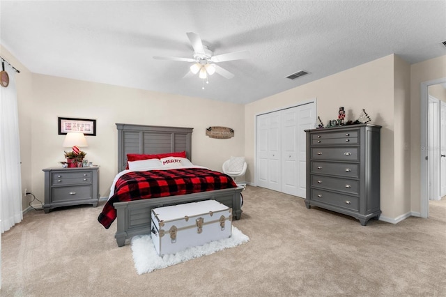 bedroom with light colored carpet, a textured ceiling, ceiling fan, and a closet