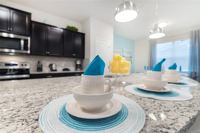 interior space with tasteful backsplash, pendant lighting, light stone countertops, and appliances with stainless steel finishes