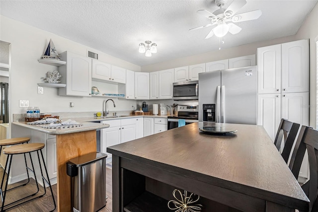 kitchen with sink, appliances with stainless steel finishes, a textured ceiling, a kitchen bar, and white cabinets