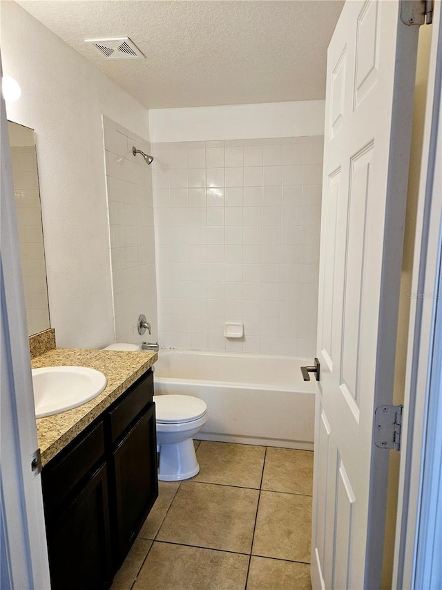 full bathroom with tiled shower / bath, tile patterned flooring, vanity, toilet, and a textured ceiling