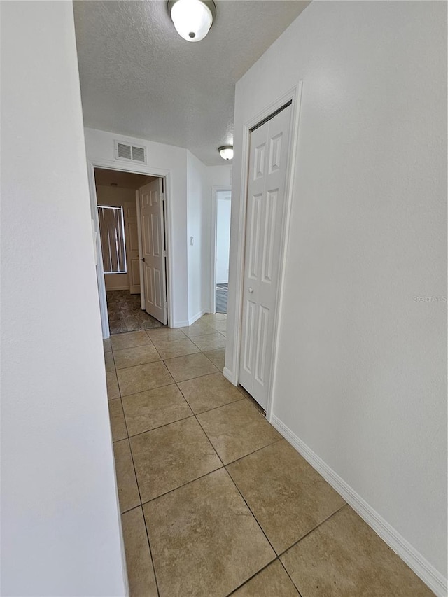 hall with light tile patterned flooring and a textured ceiling