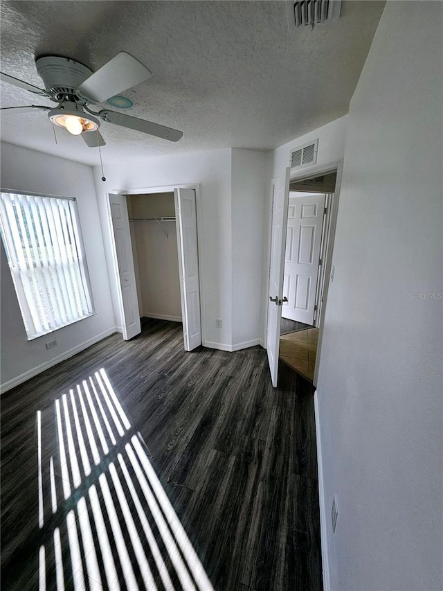 unfurnished bedroom with ceiling fan, a textured ceiling, dark hardwood / wood-style flooring, and a closet