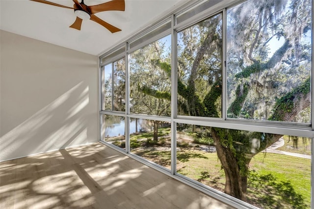 unfurnished sunroom with ceiling fan and a water view