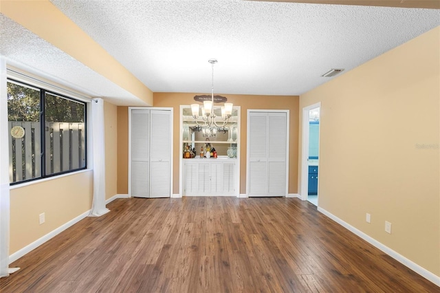 unfurnished dining area with a notable chandelier, wood-type flooring, and a textured ceiling