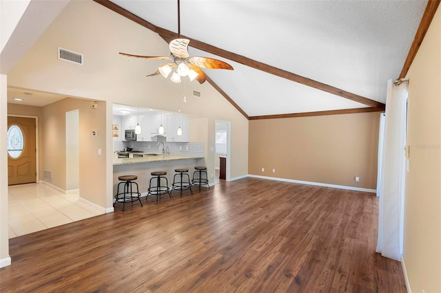 living room featuring ceiling fan, beam ceiling, sink, and light wood-type flooring