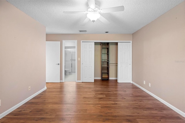 unfurnished bedroom with connected bathroom, a textured ceiling, dark hardwood / wood-style flooring, a closet, and ceiling fan