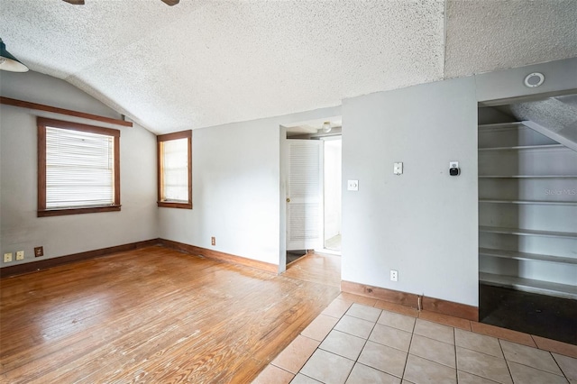 tiled empty room with built in features, lofted ceiling, and a textured ceiling