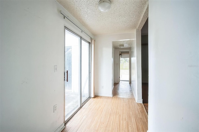 hallway with a textured ceiling and light hardwood / wood-style flooring