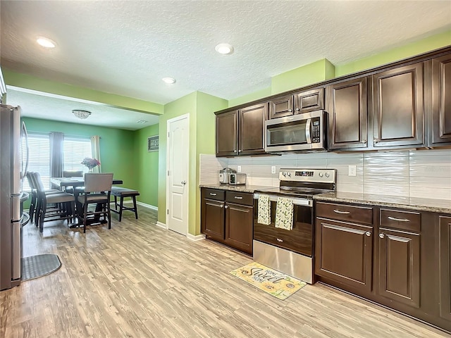 kitchen with dark brown cabinetry, stainless steel appliances, decorative backsplash, and light hardwood / wood-style flooring