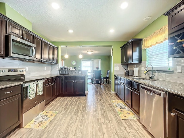 kitchen with pendant lighting, light wood-type flooring, dark brown cabinetry, and appliances with stainless steel finishes