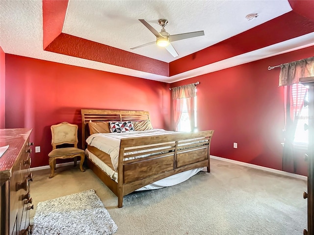 carpeted bedroom featuring a tray ceiling, a textured ceiling, and ceiling fan