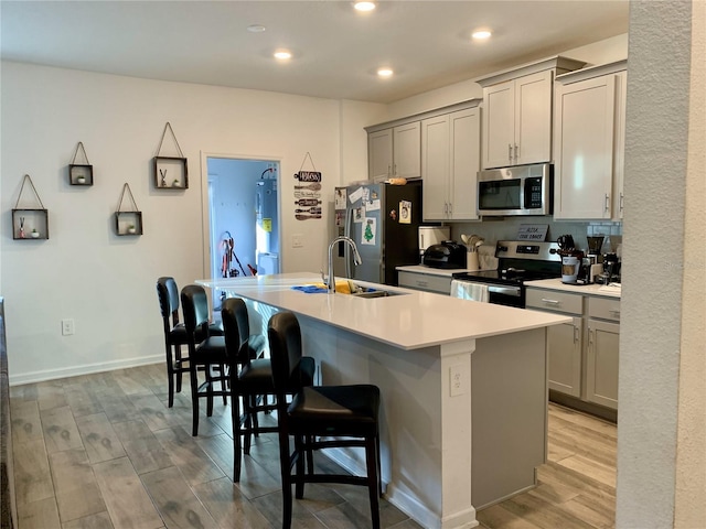 kitchen with sink, light hardwood / wood-style flooring, a breakfast bar area, appliances with stainless steel finishes, and a center island with sink