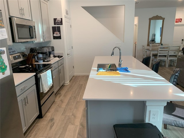 kitchen with appliances with stainless steel finishes, gray cabinets, sink, and a center island with sink