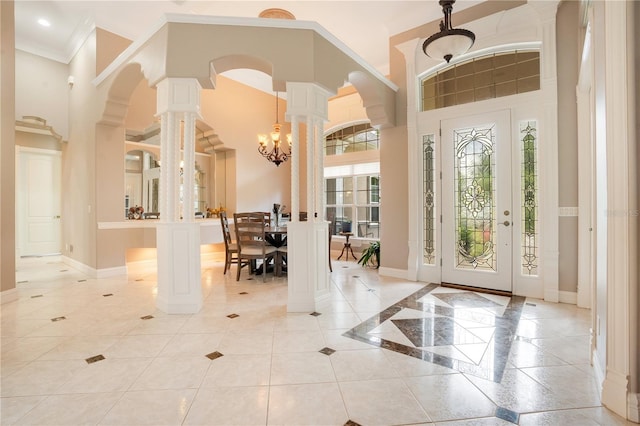 entryway featuring ornate columns, crown molding, a chandelier, and a high ceiling