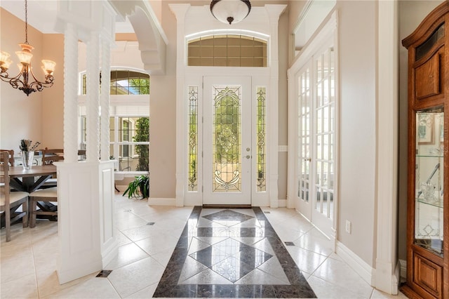 entrance foyer featuring ornate columns, a high ceiling, light tile patterned floors, and a chandelier